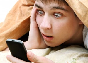 Surprised Young Man with Cellphone under Blanket on the Bed
